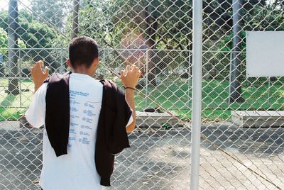 Rear view of man standing by chainlink fence
