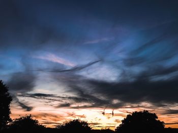 Low angle view of silhouette trees against dramatic sky