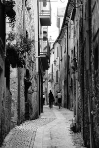 Rear view of people walking on narrow street amidst buildings