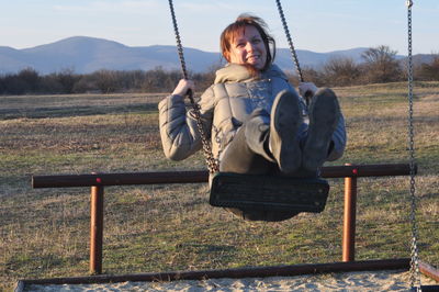 Portrait of happy woman swinging over field