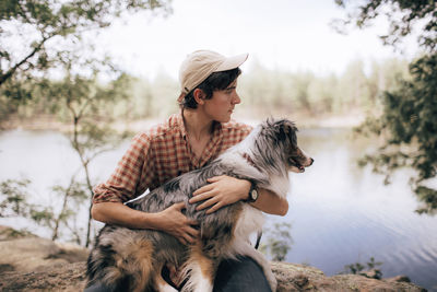 Man embracing australian shepherd while sitting on rock