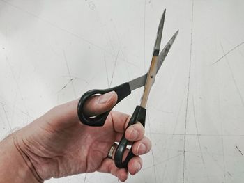 Cropped hand of man holding scissors by white wall