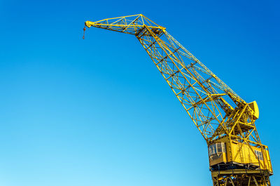 Low angle view of old yellow crane against clear blue sky