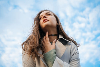 Beautiful girl with long hair in a grey trench coat blue sky background outdoors in spring