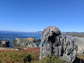 Rock formation by sea against clear blue sky