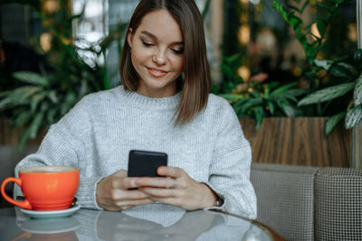 Smiling young brunette woman using smartphone in cafe