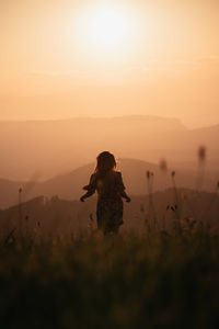 Woman standing on land against sky during sunset