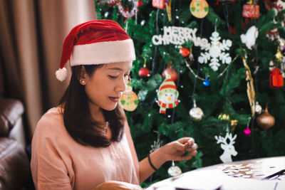 Beautiful woman in red santa hat sitting near the christmas tree