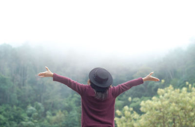 Rear view of man with arms outstretched standing against sky