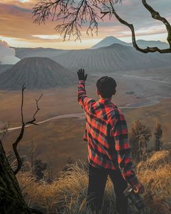 Rear view of man standing on mountain against sky during sunset