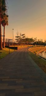 Footpath amidst trees against sky during sunset