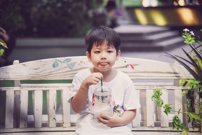 Full length of boy having drink while sitting on bench