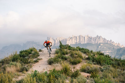 Male cyclist in helmet and sunglasses riding mountain bike among green hills in summer day