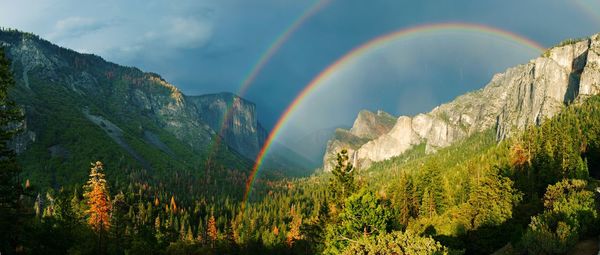 Scenic view of double rainbow and mountains against dramatic sky