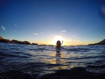 Person swimming in sea against sky during sunset