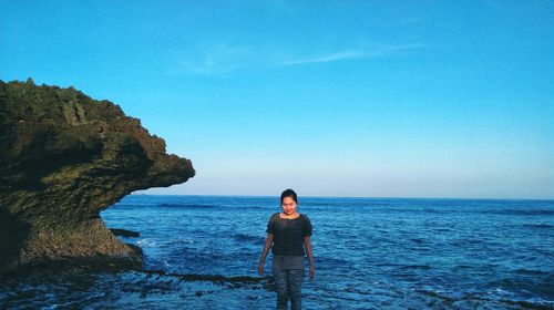 Young woman standing at beach against blue sky