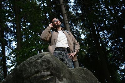 Low angle view of man talking on mobile phone while standing on rock