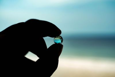 Close-up of silhouette hand holding crystal ball against sea and sky