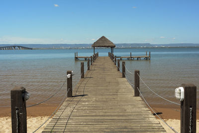 Pier leading towards gazebo amidst sea against blue sky