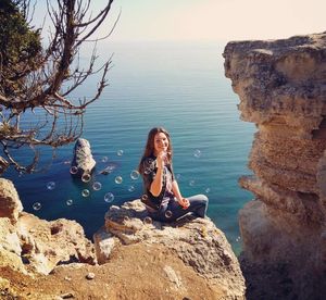 Woman blowing bubbles on rock by beach