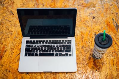 Close-up of laptop by disposable cup on table