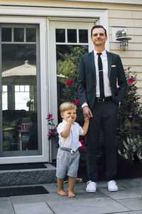 Father and son holding hands standing in front of house door
