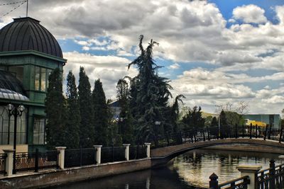 Trees in city against cloudy sky