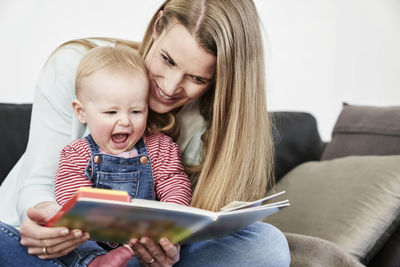 Mother and happy baby girl at home looking at book