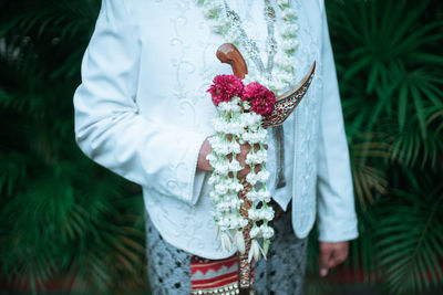 Midsection of woman holding bouquet against white wall