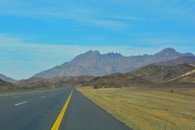 Empty road by mountains against blue sky