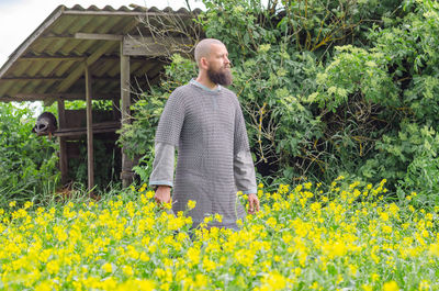 Courageous warrior man in metal chain mail with sword in middle of yellow flowers on background 