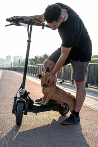 Feet of a man in sneakers made stop stand one leg with his small cute dog on electric scooter. 