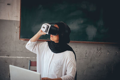 Rear view of woman using phone while standing against wall