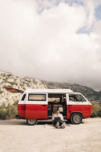 Young man using laptop while sitting near van against sky