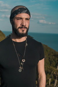 Thoughtful bearded man looking away while standing against sea