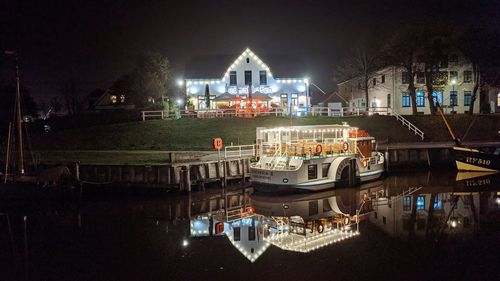 Boats moored in river against buildings at night