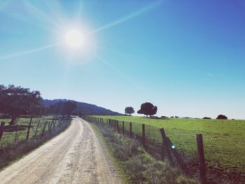 Dirt road amidst field against sky