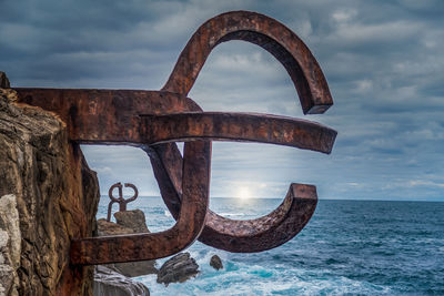 Metallic structure in sea against cloudy sky