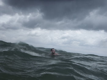 Man swimming in sea against cloudy sky during storm