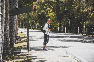 Full length portrait of young man on footpath by trees