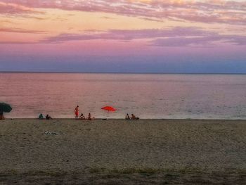 People on beach against sky during sunset