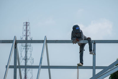 Low angle view of worker on metallic structure against sky