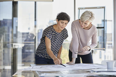 Two businesswomen discussing floor plan on desk in office