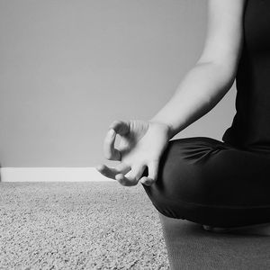 Midsection of woman meditating while sitting on floor