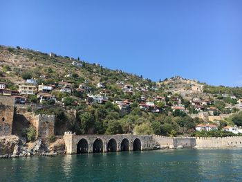 Arch bridge over river by buildings against clear sky