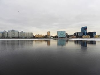 Buildings by river against sky in city