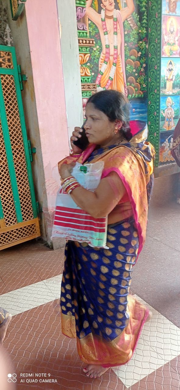 REAR VIEW OF WOMAN STANDING AGAINST TILED WALL