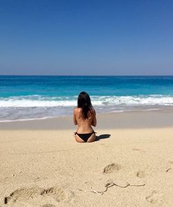 Rear view of shirtless woman sitting at beach