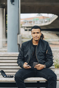 Portrait of man holding glaucometer and smart phone while sitting on bench