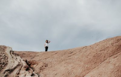 Low angle view of girl standing on mountain against cloudy sky